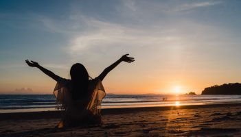 Young Asian woman watching sunset near beach, beautiful female happy relax enjoy moment when sunset in evening. Lifestyle woman travel on beach concept.